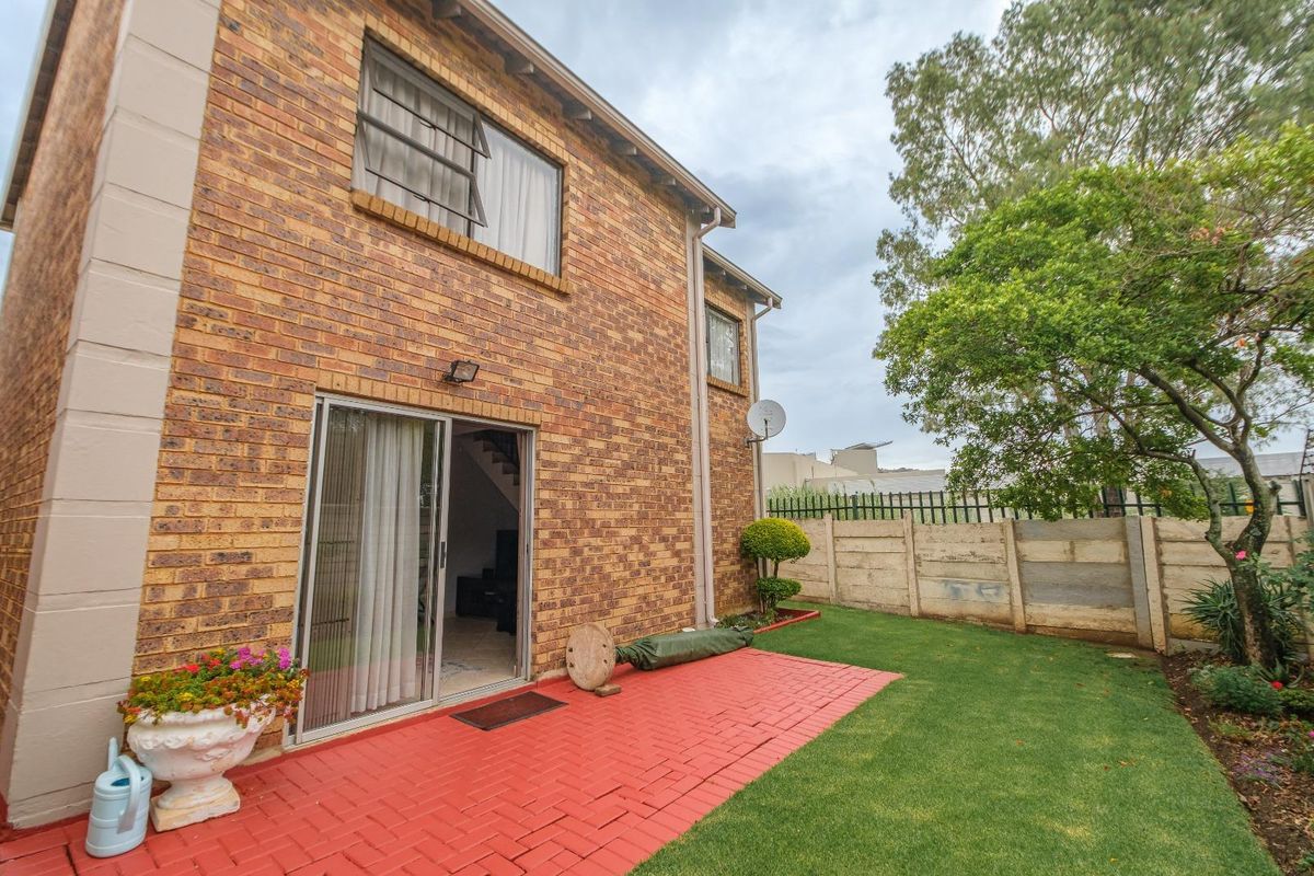 Rear view of the townhouse featuring a red brick facade, sliding glass door access, a paved patio area, and a private garden with boundary wall.