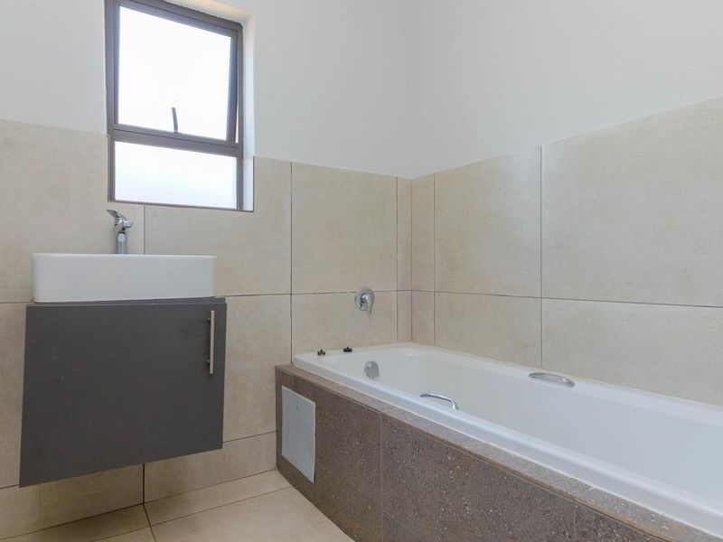 A clean, modern bathroom featuring a wall-mounted vanity with basin, a built-in bathtub, and neutral floor-to-ceiling wall tiling.