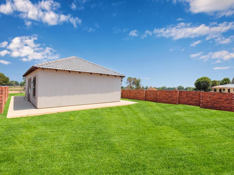 A spacious rear garden featuring a well-maintained lawn, paved patio area, and secure brick boundary walls surrounding the property.