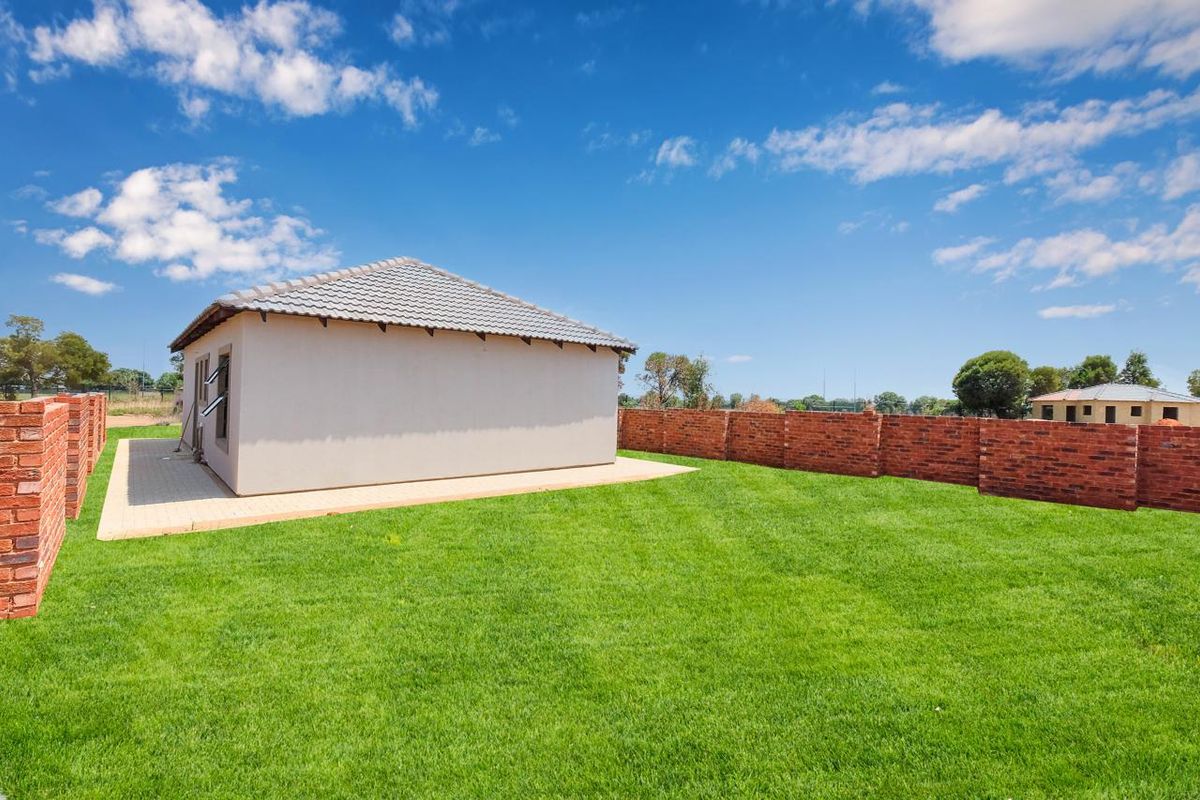 A spacious rear garden featuring a well-maintained lawn, paved patio area, and secure brick boundary walls surrounding the property.