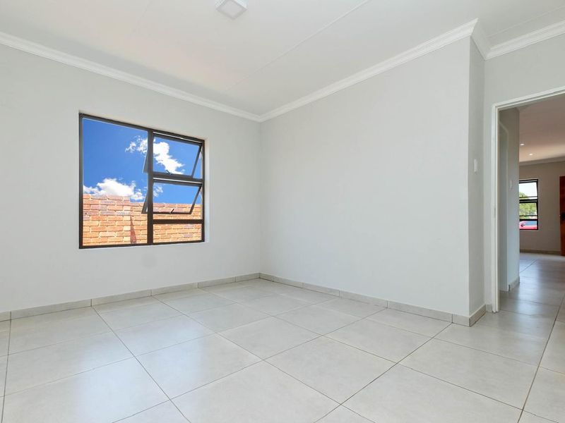 A bright, empty bedroom featuring neutral tiled flooring, clean white walls, and modern aluminium window frames.