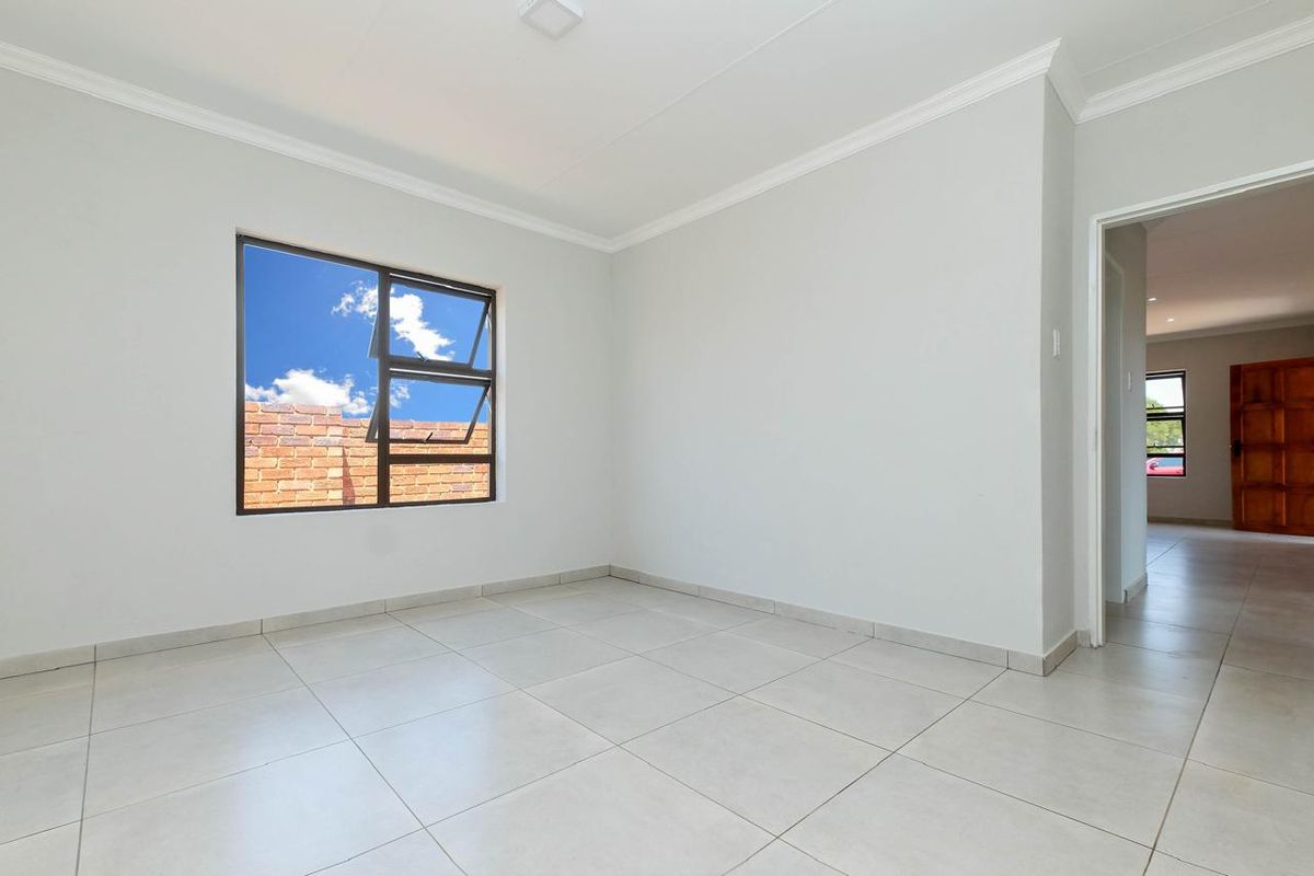 A bright, empty bedroom featuring neutral tiled flooring, clean white walls, and modern aluminium window frames.