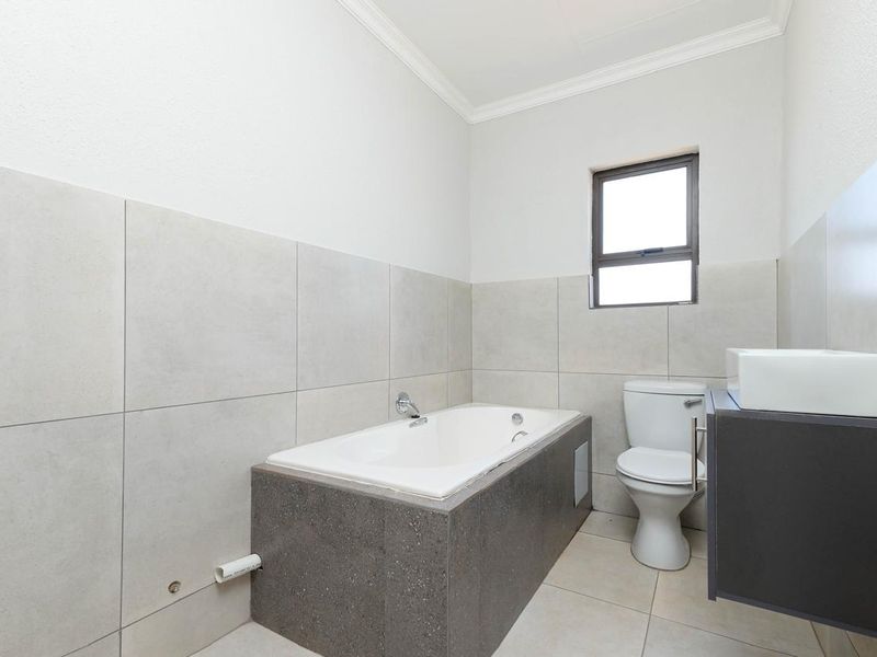 A clean, modern bathroom featuring a built-in bathtub, a vanity with basin, and neutral wall and floor tiling.
