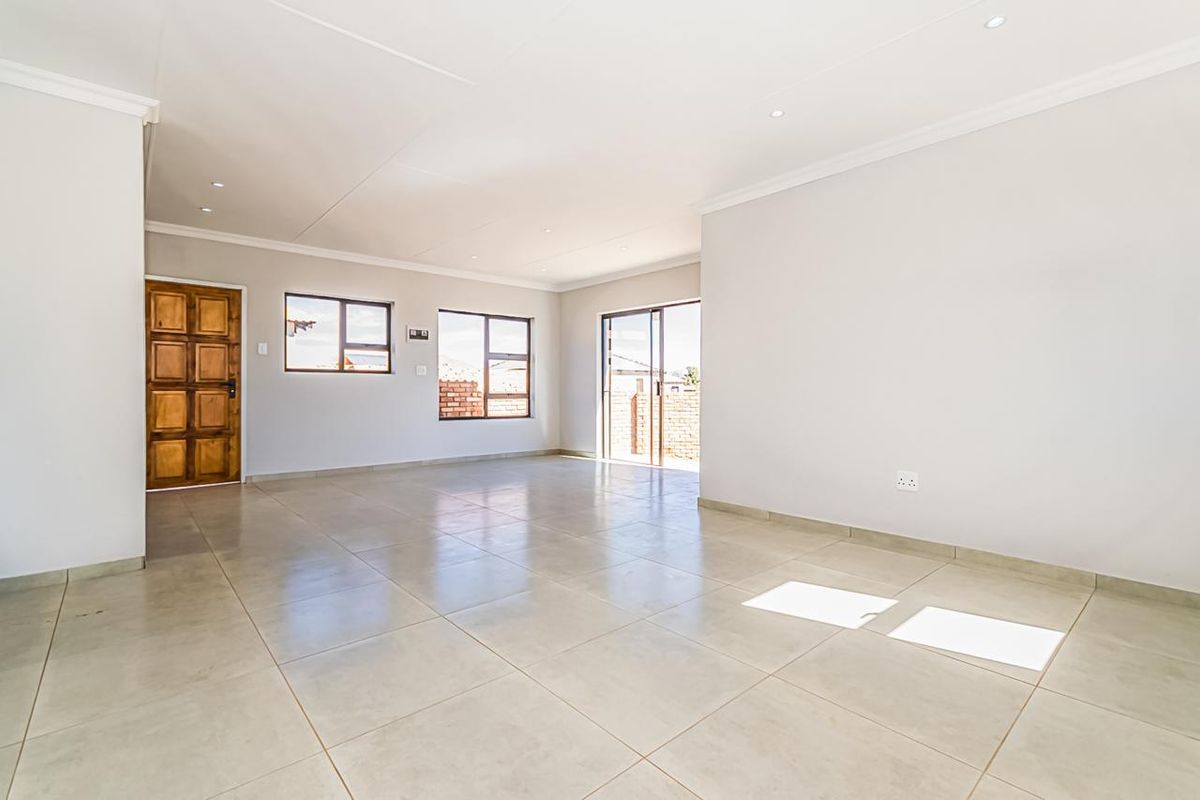 A spacious, light-filled open-plan living area featuring neutral tiled flooring, recessed downlights, and direct access to the exterior through a sliding glass door.