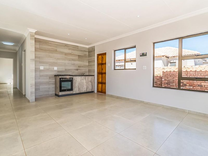 An open-plan living area featuring tiled flooring, recessed lighting, and a compact kitchen unit with a built-in oven and hob.