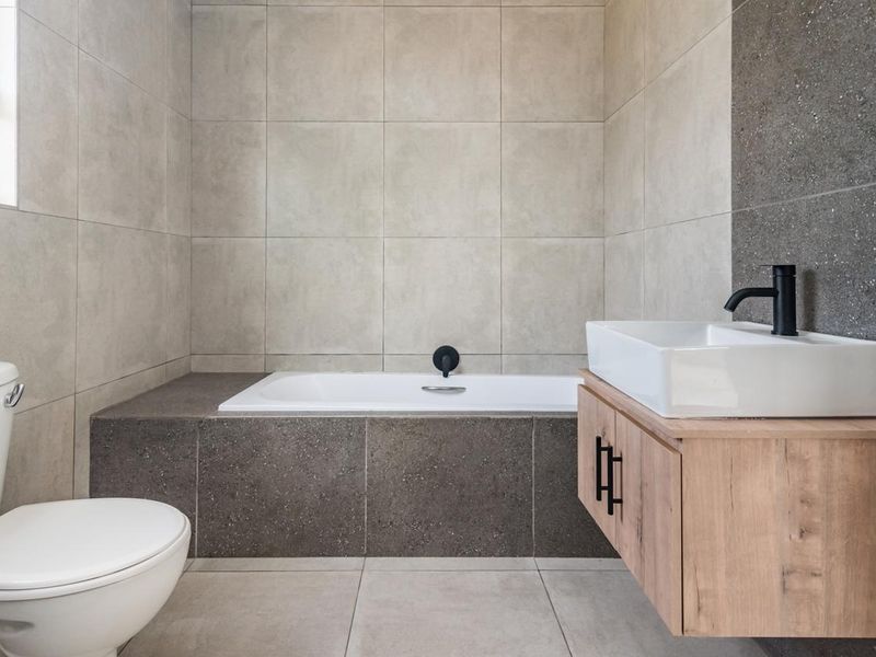 Modern bathroom featuring a built-in bathtub, wall-mounted vanity with vessel sink, and contemporary matte black fixtures with neutral tiled finishes.
