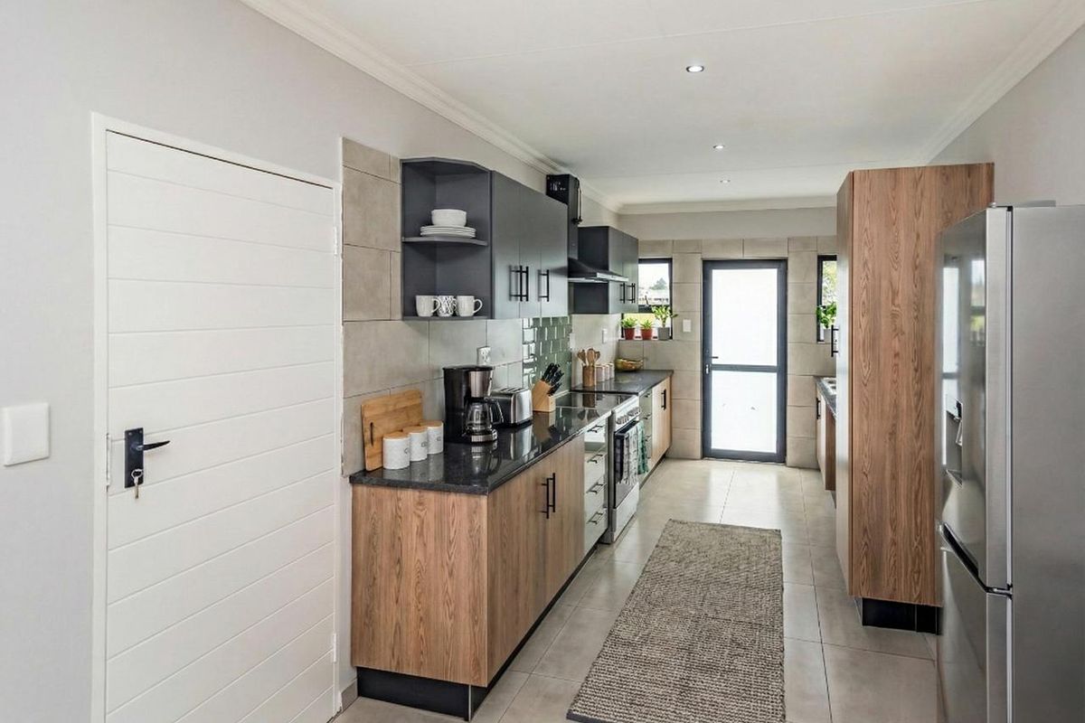 Modern galley-style kitchen featuring wood-grain cabinetry, dark stone countertops, tiled backsplash, and recessed lighting with direct access to the exterior.