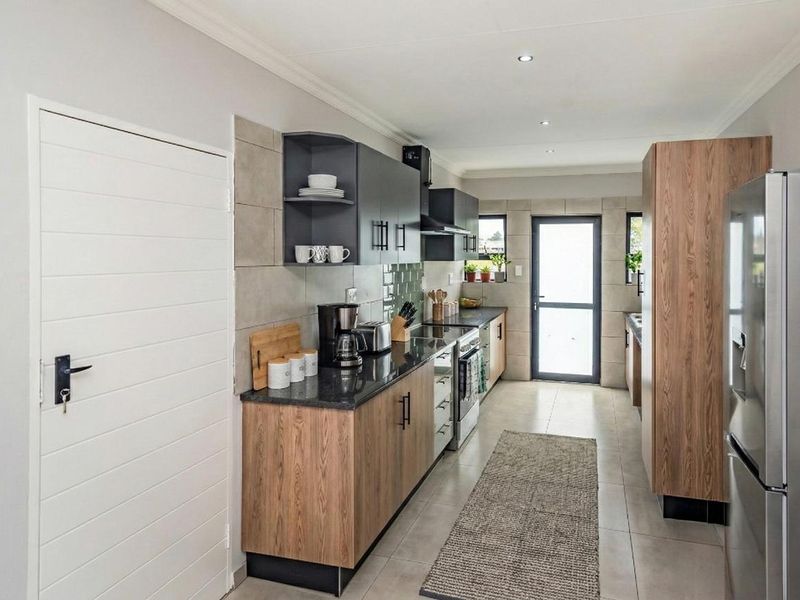 Modern galley-style kitchen featuring wood-grain cabinetry, dark stone countertops, tiled backsplash, and recessed lighting with direct access to the exterior.