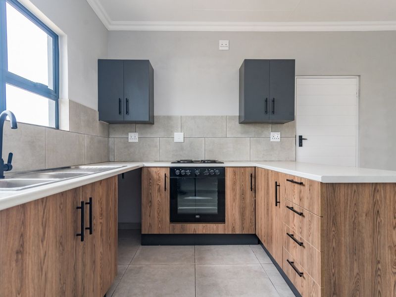 Modern kitchen featuring wood-grain cabinetry, stone countertops, built-in oven with gas hob, and neutral tiled finishes in a clean, contemporary layout.