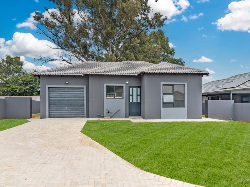 A modern single-story house featuring a grey facade, tiled roof, paved driveway, and a well-maintained front lawn.