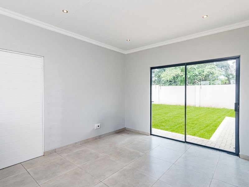 A bright, empty living room featuring neutral tiled flooring, recessed downlights, and a large sliding glass door providing direct access to the garden.