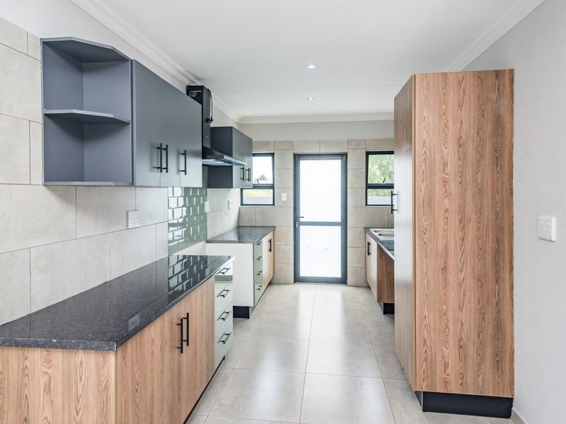 Modern kitchen featuring two-tone cabinetry, stone countertops, tiled splashbacks, and integrated extractor fan, leading to an exterior door.