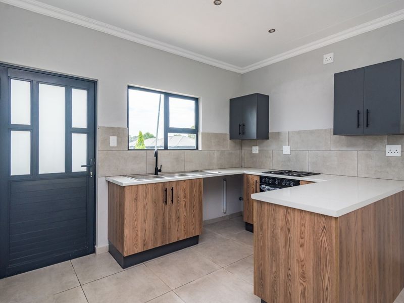 Modern kitchen featuring wood-grain cabinetry, stone countertops, a gas hob, and neutral tiled finishes, offering a clean and functional workspace.