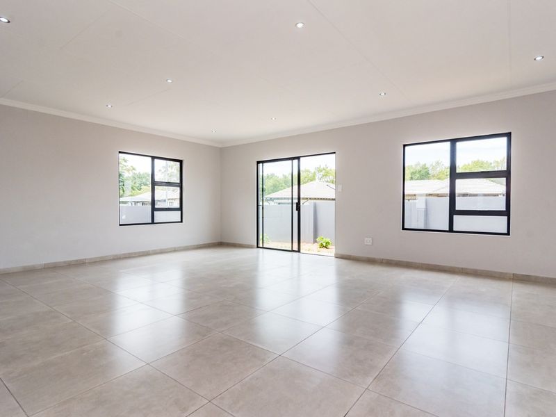 A bright, spacious, and modern open-plan living area featuring neutral tiled floors, recessed lighting, and large windows providing ample natural light.