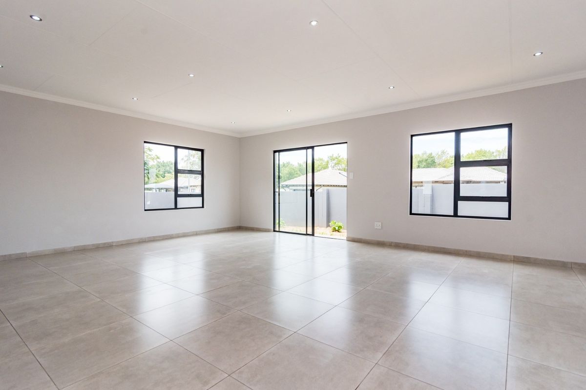 A bright, spacious, and modern open-plan living area featuring neutral tiled floors, recessed lighting, and large windows providing ample natural light.