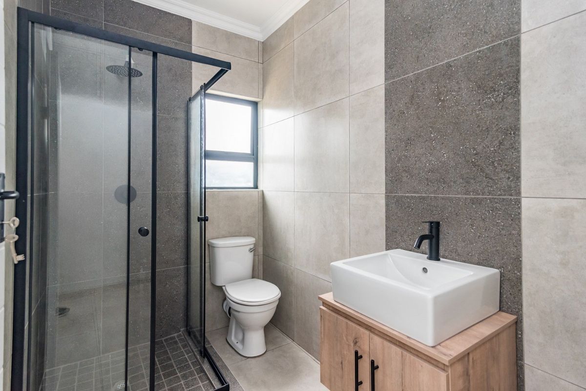 Modern bathroom featuring a walk-in shower with black frame, vessel sink on a wooden vanity, and contemporary neutral-toned wall tiling.