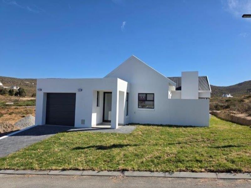 Modern single-story house featuring a clean white facade, integrated garage, and a well-maintained front lawn in a scenic landscape setting.