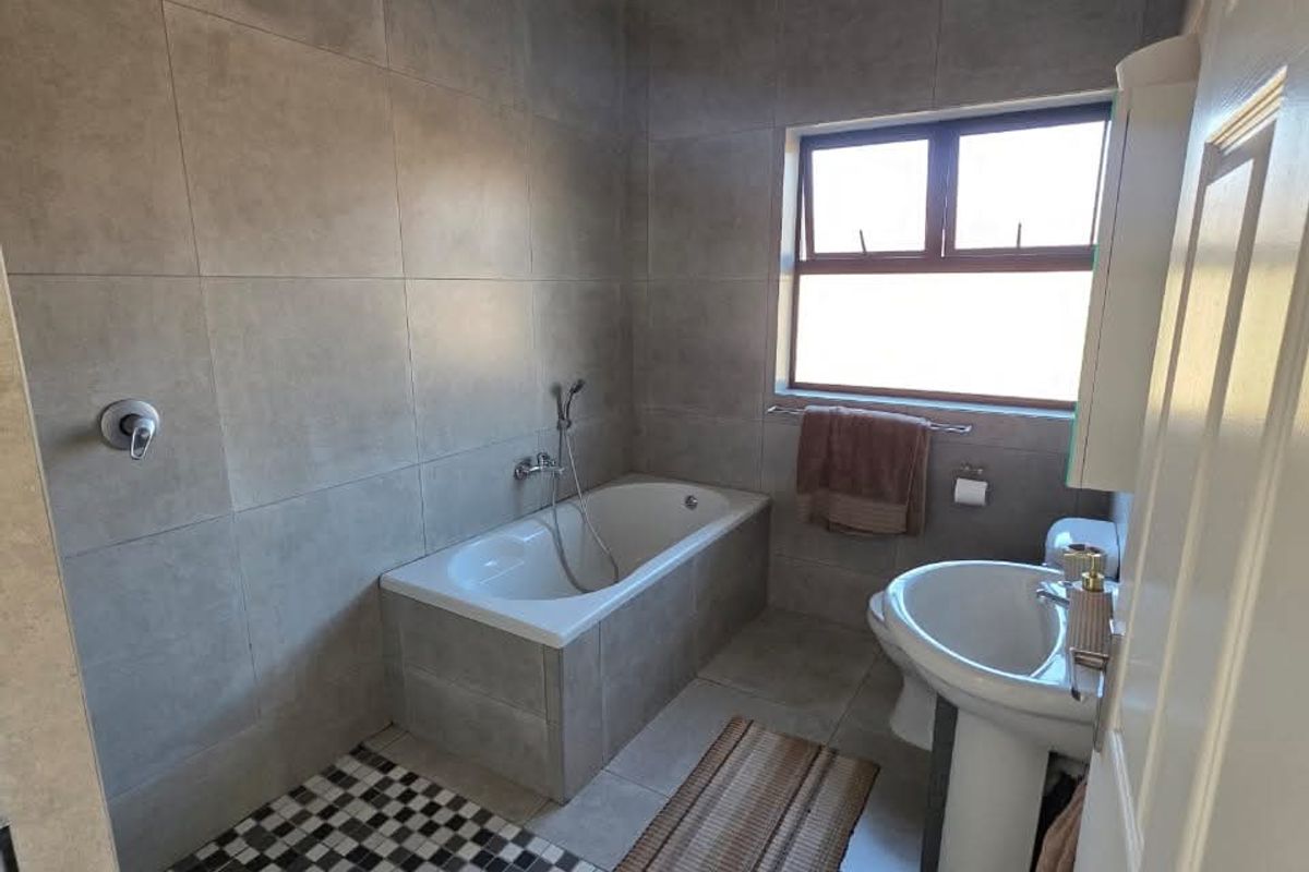 A modern bathroom featuring large format grey wall tiles, a built-in bathtub, a separate shower area with mosaic floor tiling, and a pedestal basin.
