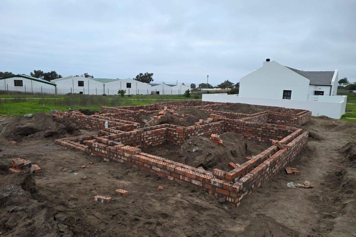 A residential property currently under construction, showing the brick foundation and initial wall structure on a cleared plot.