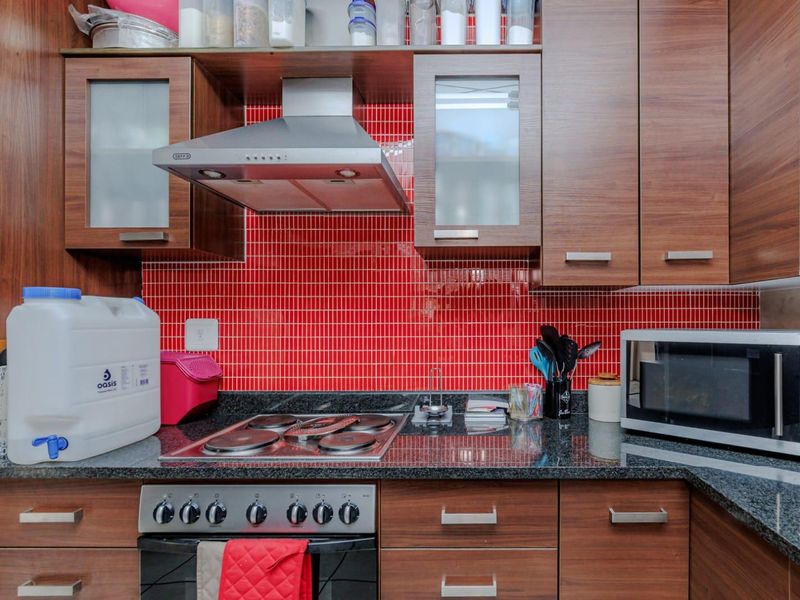 A functional kitchen featuring wood-finish cabinetry, granite countertops, a vibrant red mosaic tile backsplash, and integrated stainless steel cooking appliances.