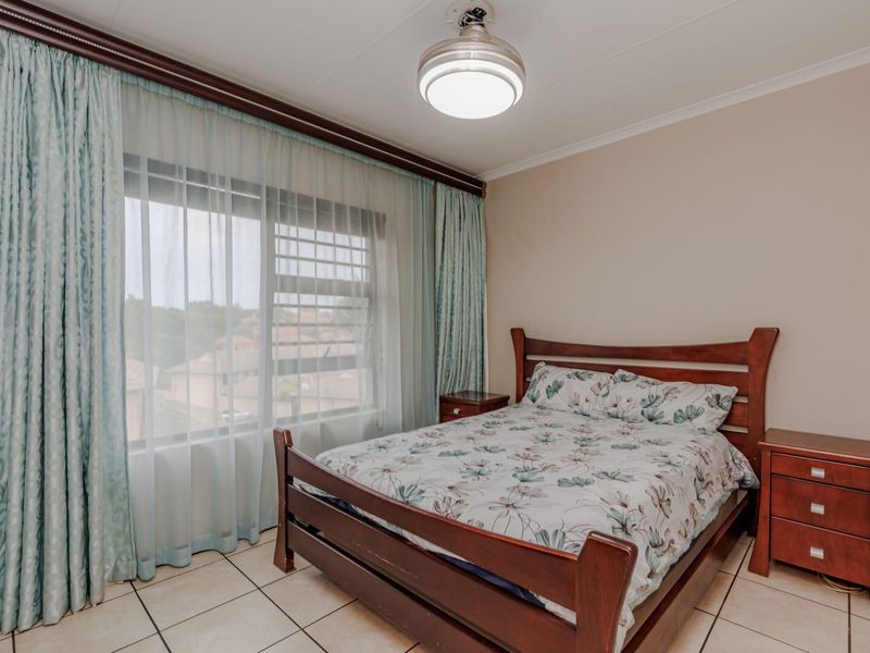 A bedroom featuring tiled flooring, a ceiling light fixture, and a large window with security bars and curtain tracks.