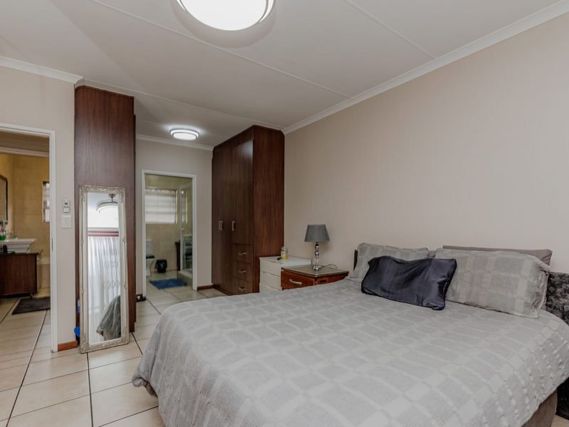 Spacious bedroom featuring built-in wooden cupboards, tiled flooring, and direct access to an en-suite bathroom.