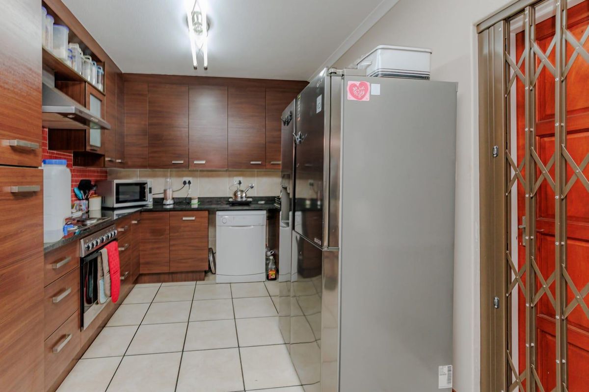 A functional kitchen featuring dark wood cabinetry, granite countertops, tiled flooring, and a built-in oven with an extractor fan.