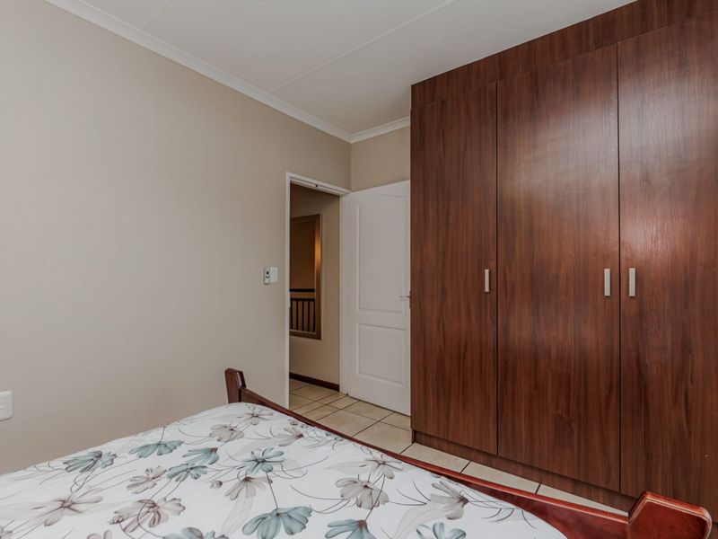 A bedroom featuring dark wood-finish built-in cupboards, neutral wall paint, and tiled flooring, providing a functional and clean living space.