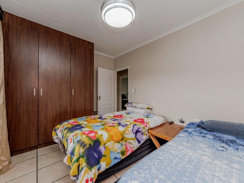 A functional bedroom featuring built-in wooden cupboards, tiled flooring, and a central ceiling light fixture.