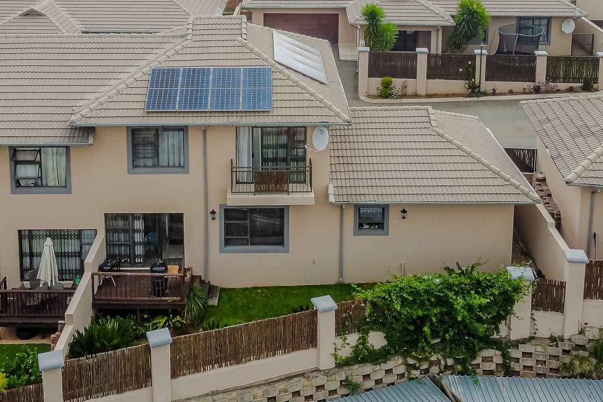 Aerial view of a townhouse featuring a tiled roof with solar panels, a small balcony, and a rear timber deck overlooking a private garden.