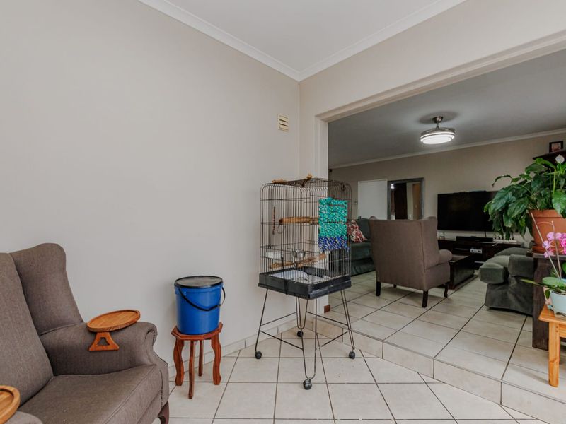 A living area featuring ceramic floor tiles and a ceiling fan, with an open-plan layout connecting to an adjacent lounge space.