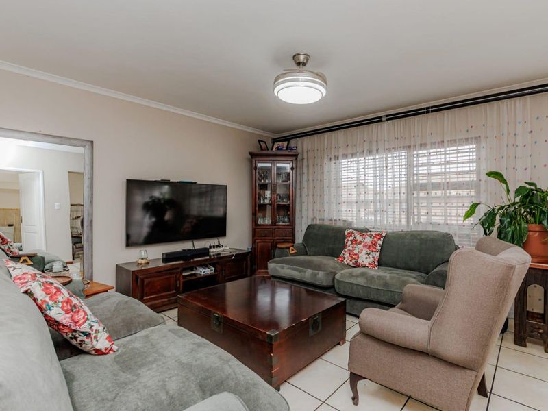 A comfortable living room featuring tiled flooring, a central ceiling fan, and large windows with curtain tracks, providing a functional and well-lit space.