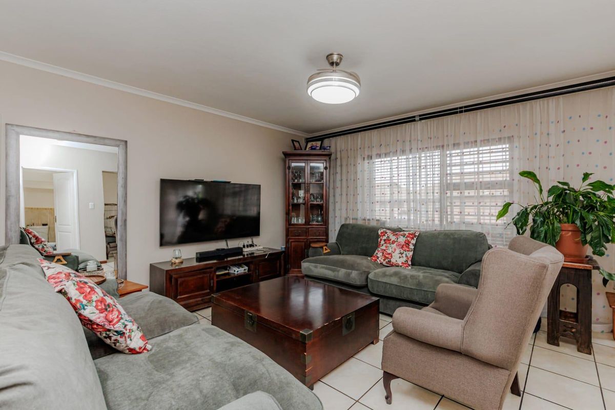 A comfortable living room featuring tiled flooring, a central ceiling fan, and large windows with curtain tracks, providing a functional and well-lit space.
