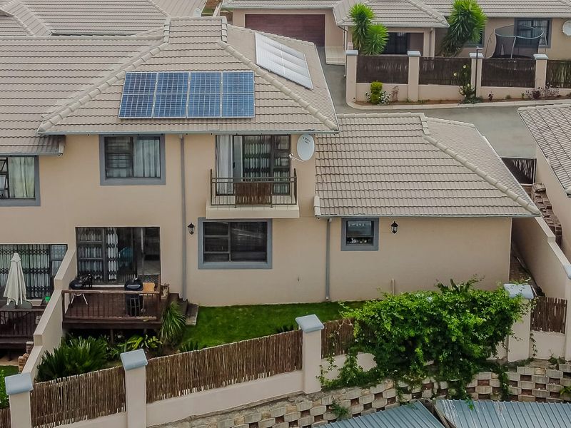 Aerial view of a townhouse featuring a tiled roof with solar panels, a small balcony, and a rear timber deck overlooking a private garden.
