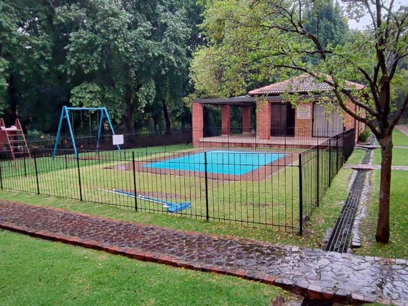 Communal pool area featuring a brick-built lapa, metal fencing, and well-maintained lawn within an apartment complex setting.