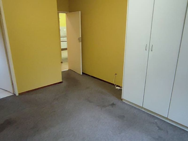 An empty bedroom featuring built-in cupboards, carpeted flooring, and an adjoining bathroom with a pedestal basin.
