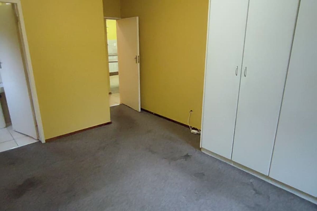 An empty bedroom featuring built-in cupboards, carpeted flooring, and an adjoining bathroom with a pedestal basin.