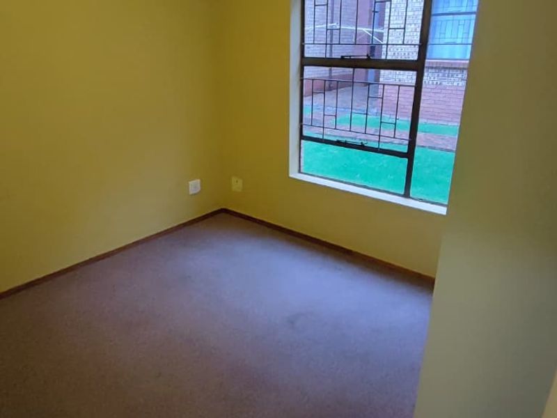 An empty bedroom featuring carpeted flooring, yellow painted walls, and a window fitted with security bars.