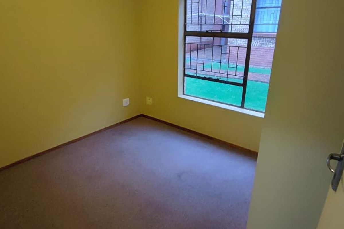 An empty bedroom featuring carpeted flooring, yellow painted walls, and a window fitted with security bars.
