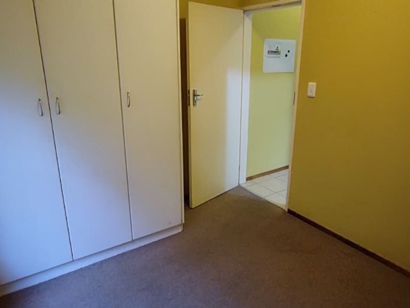 An empty bedroom featuring built-in cupboards, carpeted flooring, and access to an adjacent hallway.