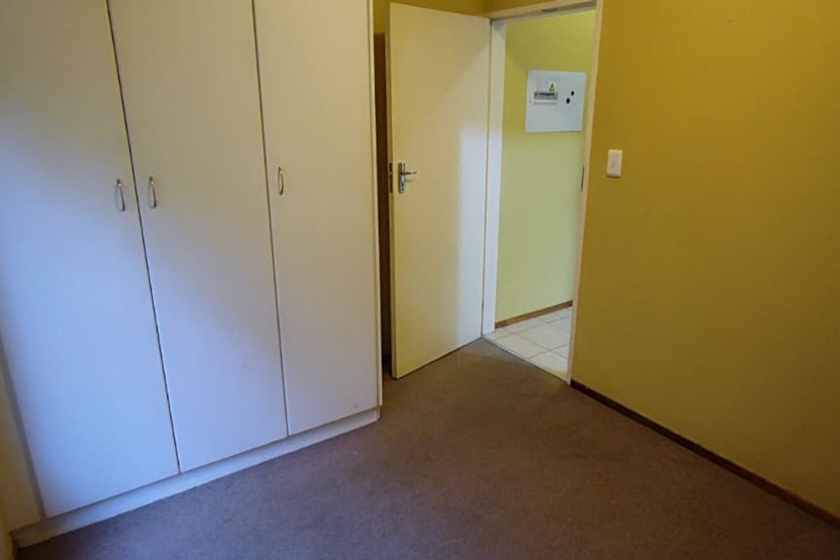 An empty bedroom featuring built-in cupboards, carpeted flooring, and access to an adjacent hallway.