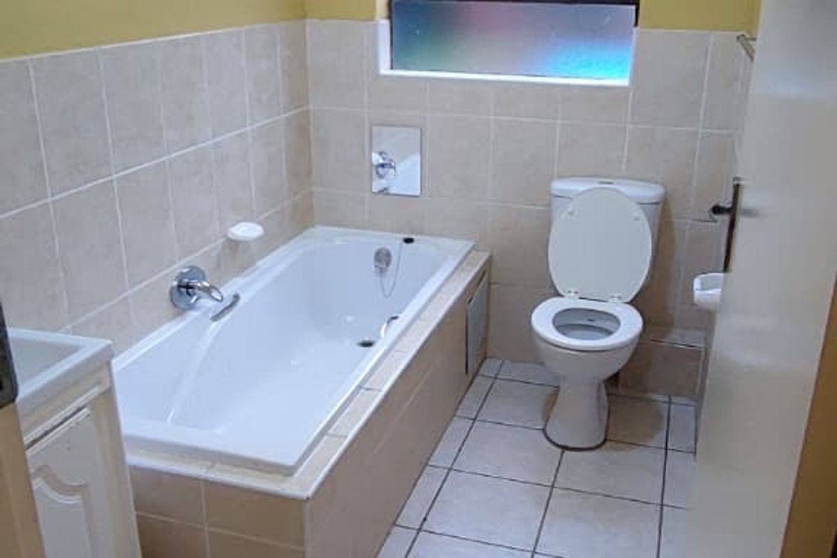 A functional bathroom featuring a built-in bathtub, toilet, and vanity cabinet with neutral wall and floor tiling.