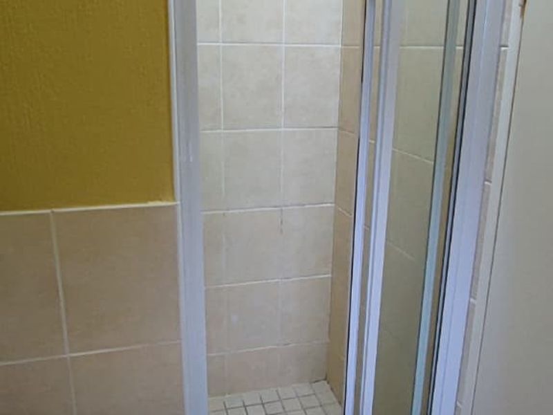A compact bathroom featuring a shower enclosure with a glass door, a pedestal basin, and tiled finishes throughout.