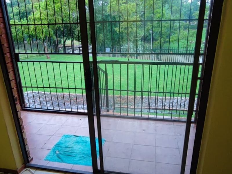 A covered patio area featuring tiled flooring, a sliding glass door, and security gate, providing direct access to a garden space.