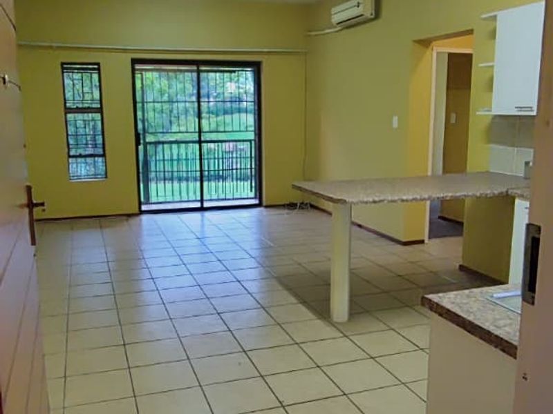 Spacious open-plan living and kitchen area featuring tiled flooring, a breakfast bar, and a sliding glass door leading to a balcony.