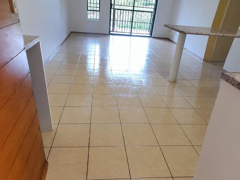 Spacious open-plan living area featuring neutral ceramic floor tiles, a breakfast bar, and a sliding glass door leading to an outdoor balcony.