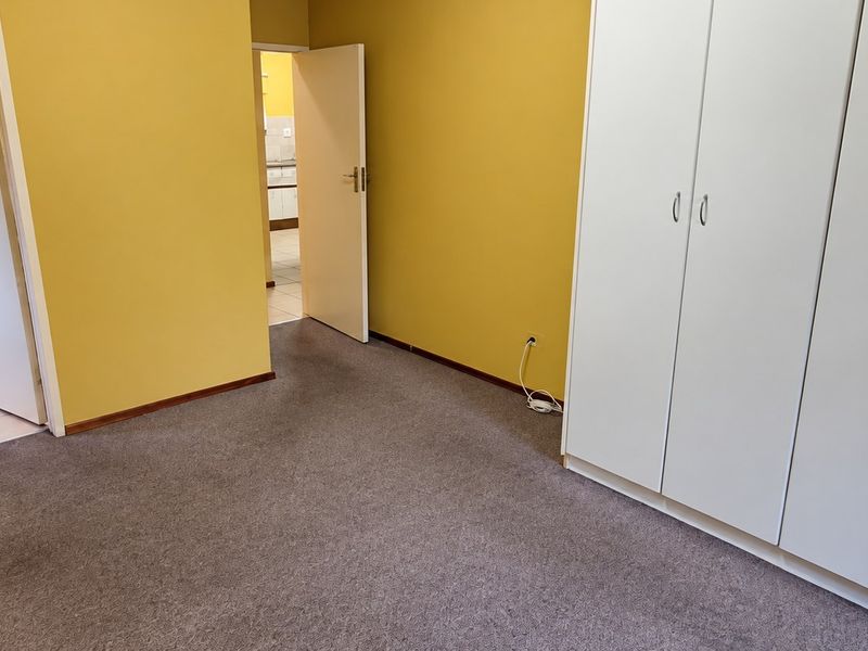 A spacious bedroom featuring built-in cupboards, carpeted flooring, and an en-suite bathroom with a pedestal basin.