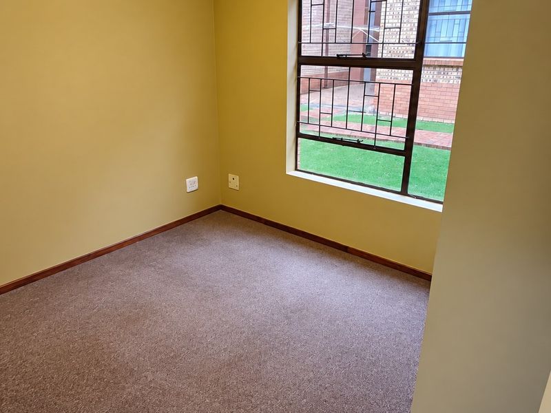 A clean, empty bedroom featuring neutral wall paint, carpeted flooring, and a window fitted with security bars.
