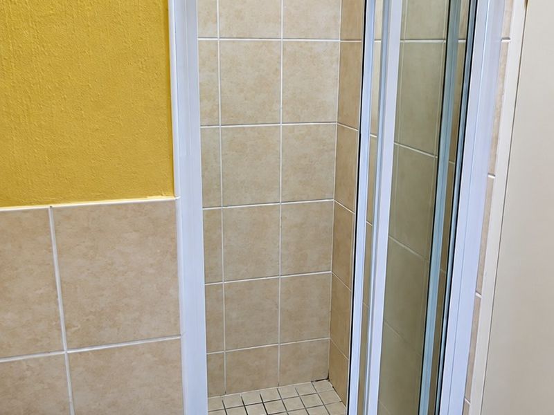 A functional bathroom featuring a shower enclosure with sliding doors, a pedestal basin, and neutral wall and floor tiling.