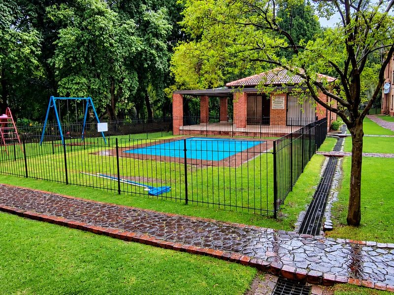 Communal pool area featuring a brick-built lapa, metal fencing, and landscaped garden surroundings within an apartment complex.